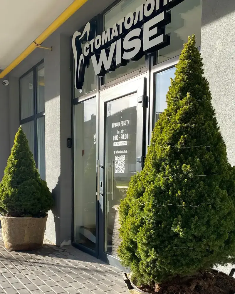 Вхід до клініки з вивіскою «Стоматологія WISE» і туями в горщиках